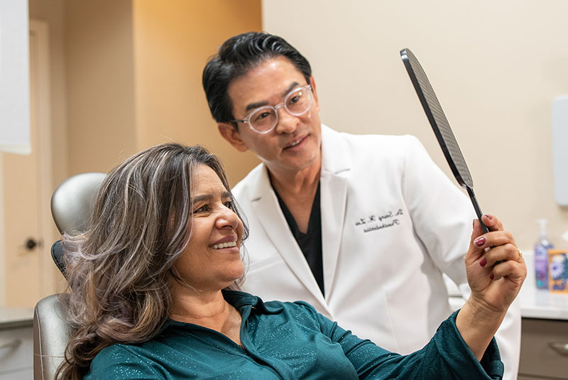 patient and doctor both smiling while looking in the mirror after dental procedure