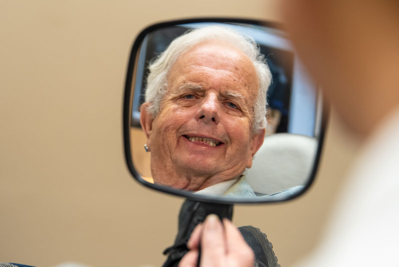 headshot of patient smiling brightly while looking within a mirror